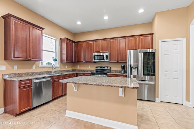 kitchen with appliances with stainless steel finishes, a breakfast bar, light stone countertops, a center island, and sink