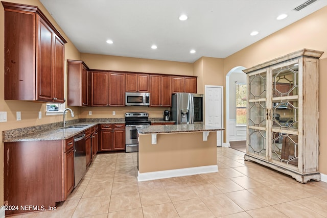 kitchen featuring light stone countertops, stainless steel appliances, a kitchen bar, a center island, and sink