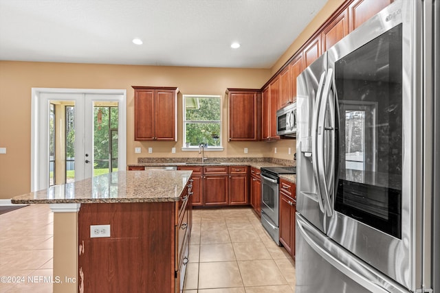 kitchen featuring a center island, stainless steel appliances, light tile patterned floors, light stone countertops, and french doors