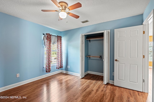 unfurnished bedroom with ceiling fan, a textured ceiling, light wood-type flooring, and multiple windows