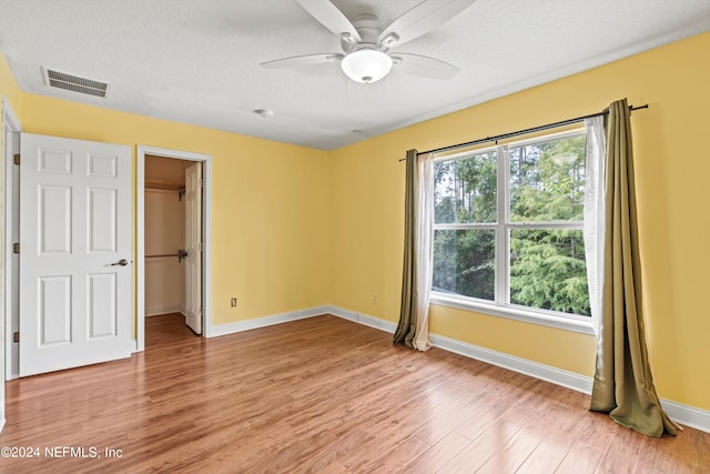 interior space with a spacious closet, a closet, light wood-type flooring, a textured ceiling, and ceiling fan