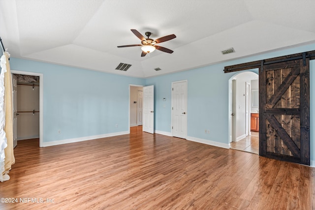 unfurnished bedroom featuring vaulted ceiling, light hardwood / wood-style floors, ceiling fan, and a barn door