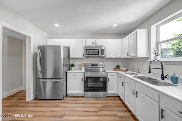 kitchen with light stone counters, light hardwood / wood-style floors, sink, white cabinetry, and appliances with stainless steel finishes