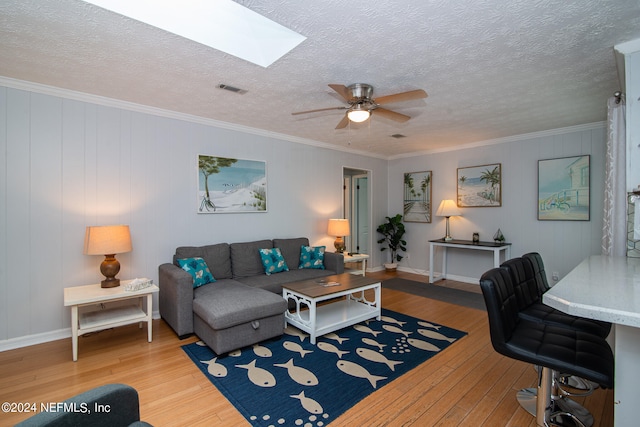 living room featuring ceiling fan, a skylight, crown molding, and light hardwood / wood-style floors