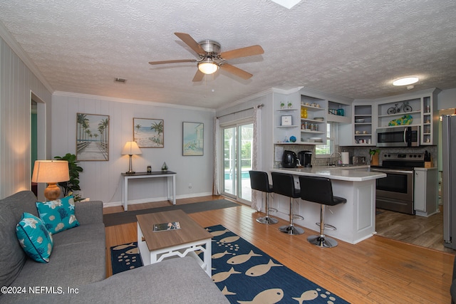 living room featuring ceiling fan, sink, wood-type flooring, a textured ceiling, and crown molding