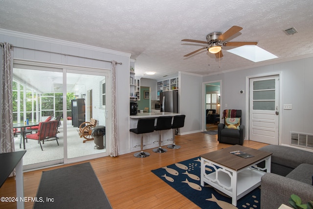 living room with wood-type flooring, a textured ceiling, ornamental molding, and ceiling fan