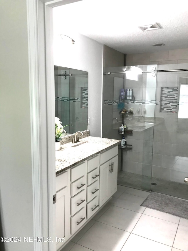 bathroom featuring vanity, a shower with shower door, tile patterned flooring, and a textured ceiling