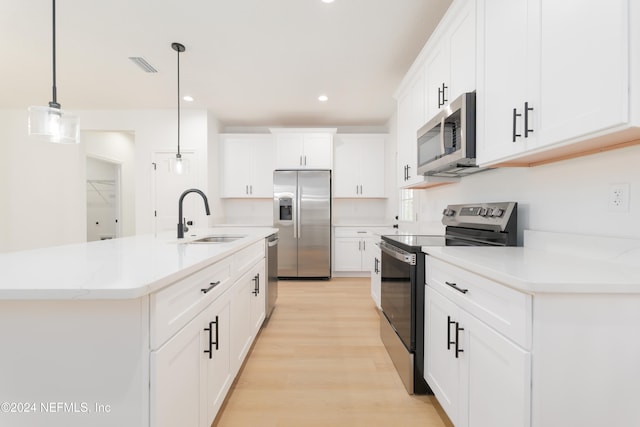 kitchen with sink, a kitchen island with sink, white cabinetry, appliances with stainless steel finishes, and decorative light fixtures