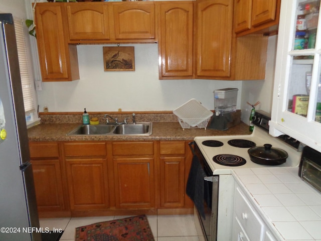 kitchen featuring stainless steel refrigerator, sink, white electric range oven, tile countertops, and light tile patterned flooring