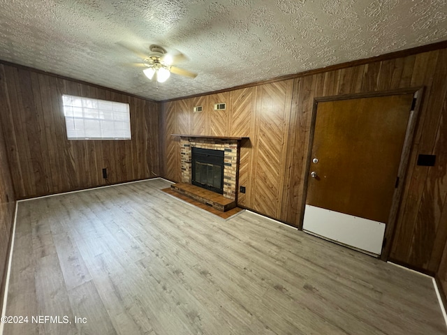 unfurnished living room with light hardwood / wood-style flooring, wooden walls, ceiling fan, and a textured ceiling