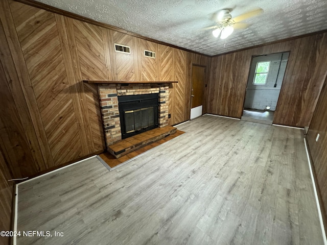 unfurnished living room with light hardwood / wood-style flooring, wood walls, ceiling fan, and a fireplace