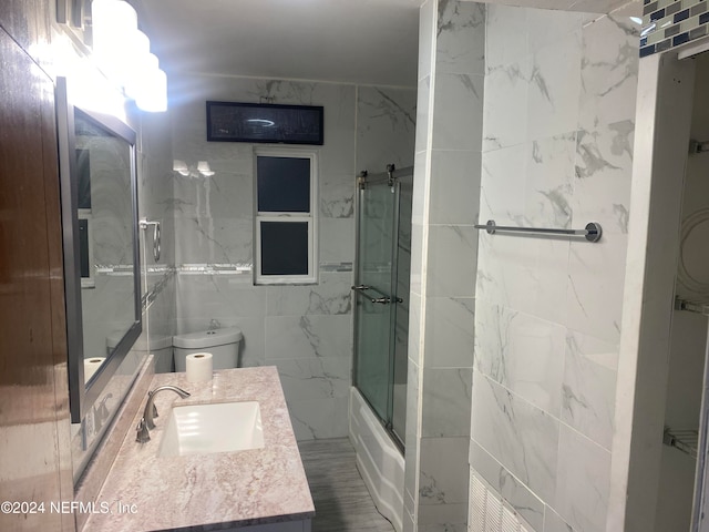 full bathroom featuring vanity, combined bath / shower with glass door, toilet, and tile walls