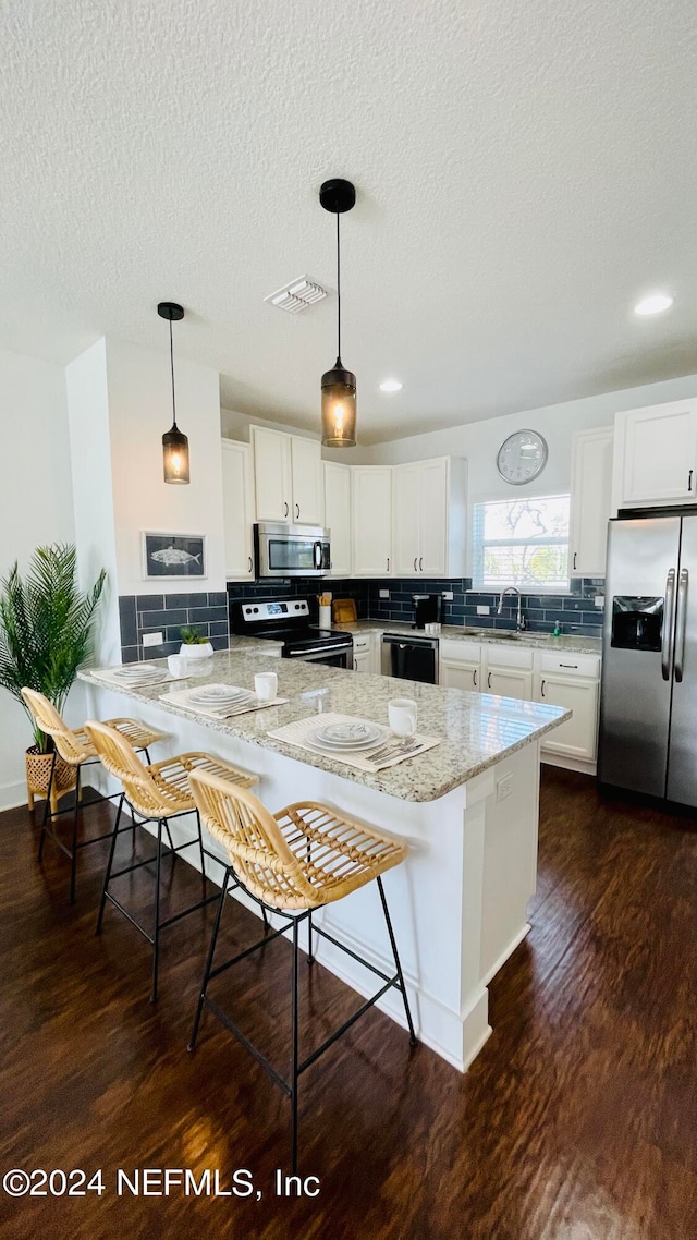 kitchen featuring appliances with stainless steel finishes, white cabinets, a kitchen bar, and decorative light fixtures