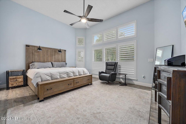 bedroom with a high ceiling, ceiling fan, hardwood / wood-style floors, and a textured ceiling