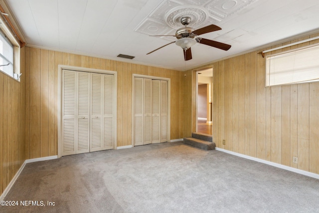 unfurnished bedroom featuring ceiling fan, multiple closets, carpet floors, and wooden walls