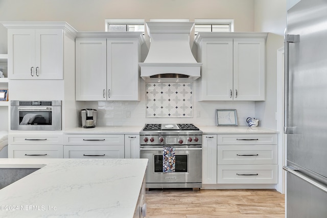 kitchen with white cabinetry, tasteful backsplash, light hardwood / wood-style flooring, custom exhaust hood, and high quality appliances