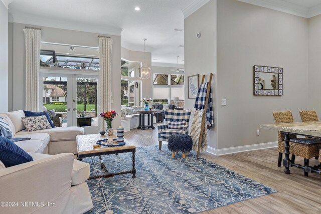 living room with french doors, ornamental molding, light wood-type flooring, and a chandelier