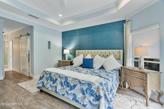 bedroom with wood-type flooring, ceiling fan, crown molding, and a barn door