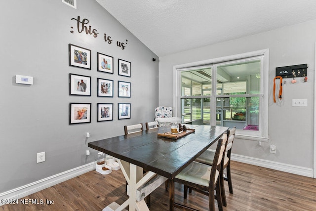 dining room with hardwood / wood-style flooring, vaulted ceiling, and a textured ceiling