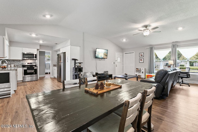 dining space featuring ceiling fan, sink, a textured ceiling, light hardwood / wood-style flooring, and vaulted ceiling