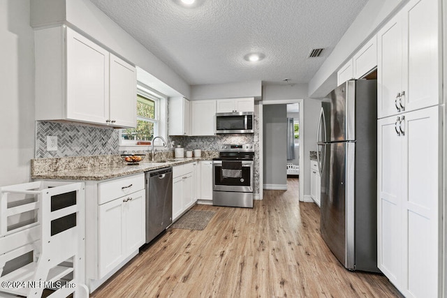 kitchen featuring light stone counters, light hardwood / wood-style floors, a textured ceiling, white cabinetry, and appliances with stainless steel finishes