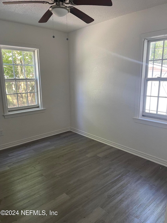 empty room with a wealth of natural light, ceiling fan, and dark wood-type flooring