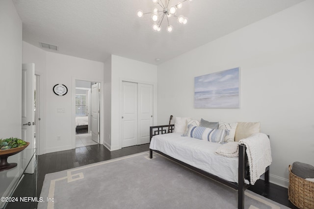 bedroom with a textured ceiling, a closet, dark hardwood / wood-style floors, and an inviting chandelier