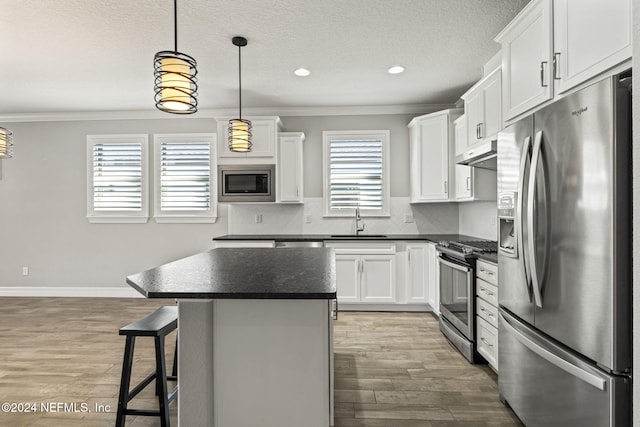 kitchen featuring ornamental molding, stainless steel appliances, pendant lighting, a center island, and white cabinetry