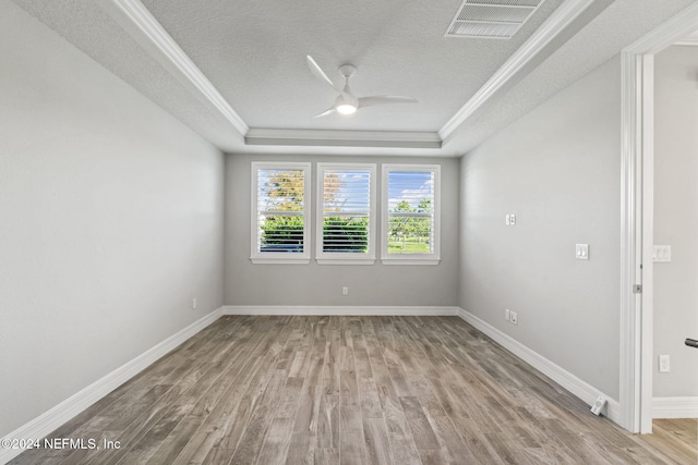 empty room featuring a textured ceiling, light wood-type flooring, a tray ceiling, and ceiling fan