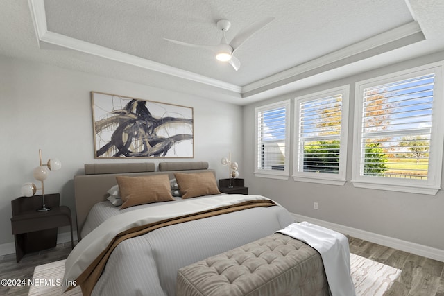 bedroom with a raised ceiling, ceiling fan, hardwood / wood-style floors, and a textured ceiling