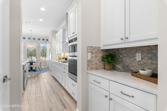 kitchen featuring backsplash, hanging light fixtures, light hardwood / wood-style flooring, light stone countertops, and white cabinetry