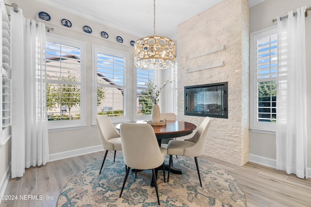 dining area with ornamental molding, light hardwood / wood-style flooring, a stone fireplace, and a healthy amount of sunlight