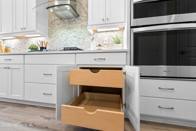 kitchen featuring decorative backsplash, light wood-type flooring, black electric cooktop, range hood, and white cabinetry