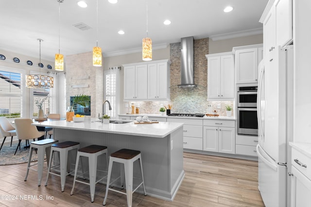 kitchen with pendant lighting, white cabinetry, wall chimney exhaust hood, and sink