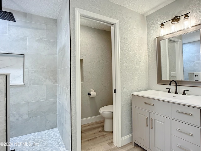 bathroom featuring a tile shower, toilet, a textured ceiling, and hardwood / wood-style floors