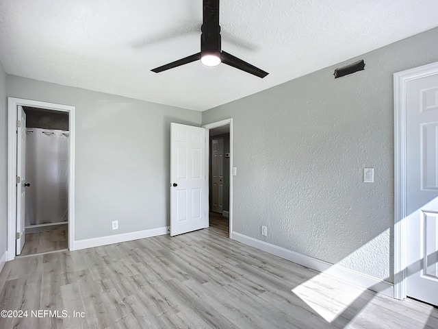 unfurnished bedroom featuring a closet, ceiling fan, light hardwood / wood-style flooring, and a walk in closet