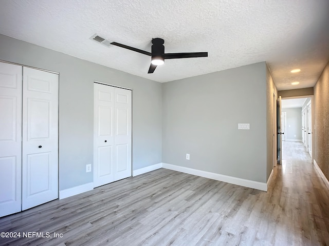 unfurnished bedroom featuring two closets, a textured ceiling, light wood-type flooring, and ceiling fan