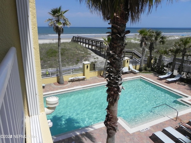 view of swimming pool featuring a patio, a water view, and a view of the beach