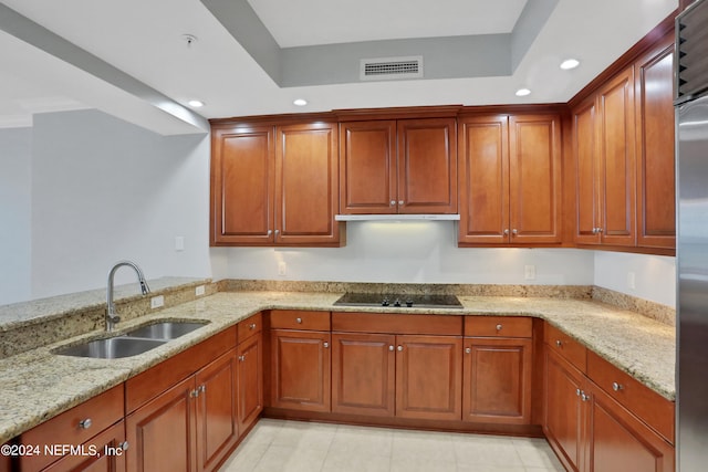 kitchen with a raised ceiling, kitchen peninsula, light stone countertops, black electric stovetop, and sink