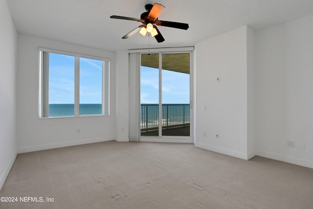 empty room with light carpet, a water view, ceiling fan, and a textured ceiling