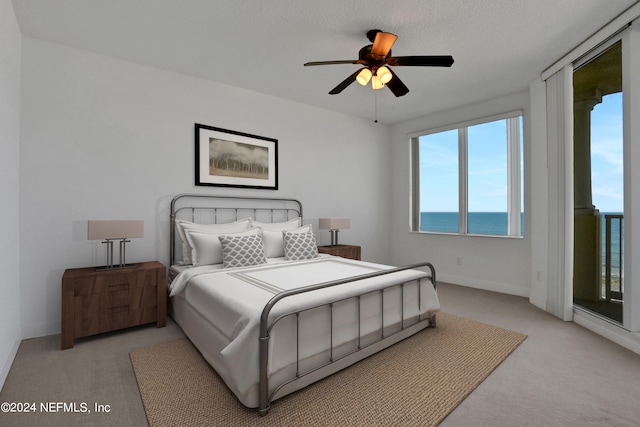 carpeted bedroom featuring a water view, ceiling fan, access to outside, and a textured ceiling