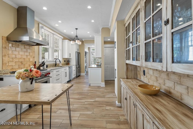 kitchen featuring sink, wall chimney range hood, light stone counters, backsplash, and decorative light fixtures