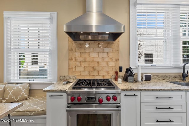 kitchen with light stone countertops, sink, high end range, ventilation hood, and white cabinets