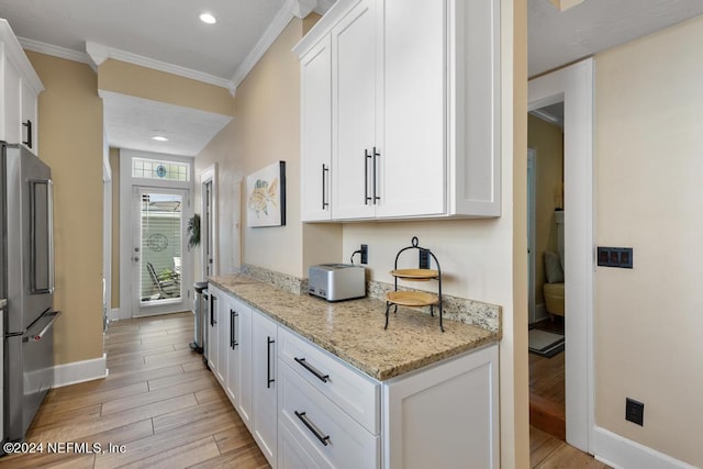 kitchen featuring stainless steel refrigerator, light stone counters, white cabinets, and ornamental molding