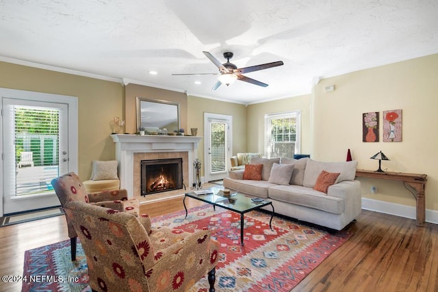 living room featuring a tiled fireplace, crown molding, hardwood / wood-style floors, and a healthy amount of sunlight