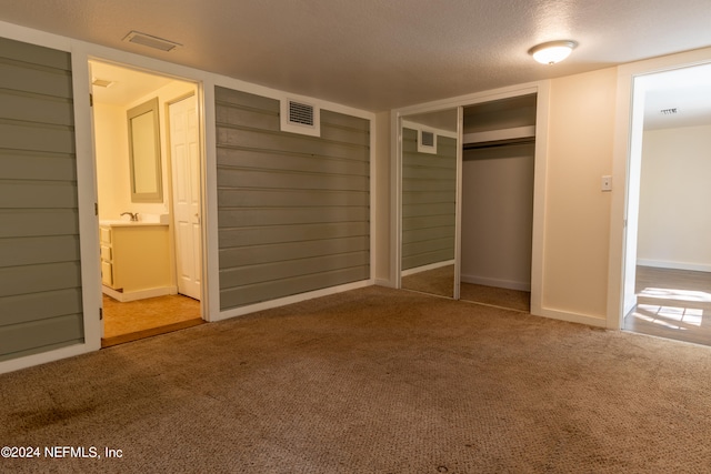 unfurnished bedroom with a textured ceiling, a closet, ensuite bath, and carpet