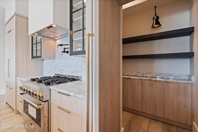 kitchen with decorative light fixtures, exhaust hood, stainless steel stove, decorative backsplash, and light stone counters