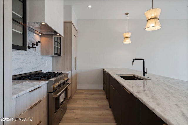 kitchen featuring pendant lighting, wall chimney exhaust hood, double oven range, sink, and light stone counters