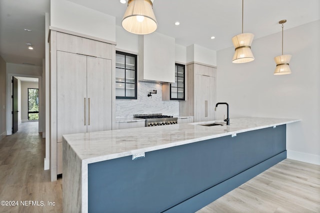 kitchen with sink, hanging light fixtures, backsplash, light stone counters, and stove