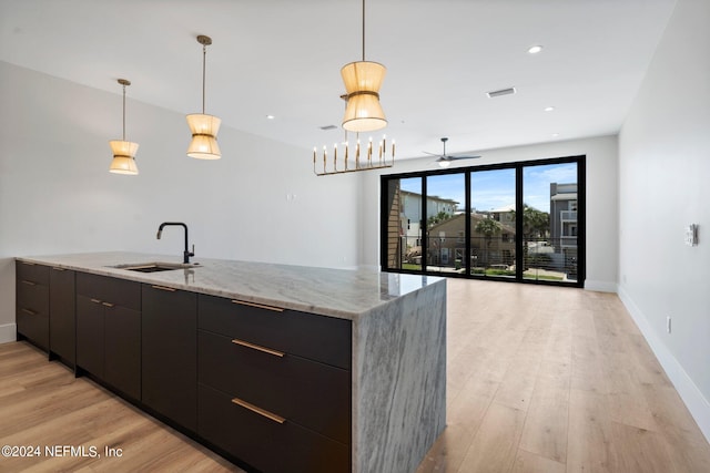 kitchen featuring decorative light fixtures, ceiling fan, sink, light stone counters, and light hardwood / wood-style flooring